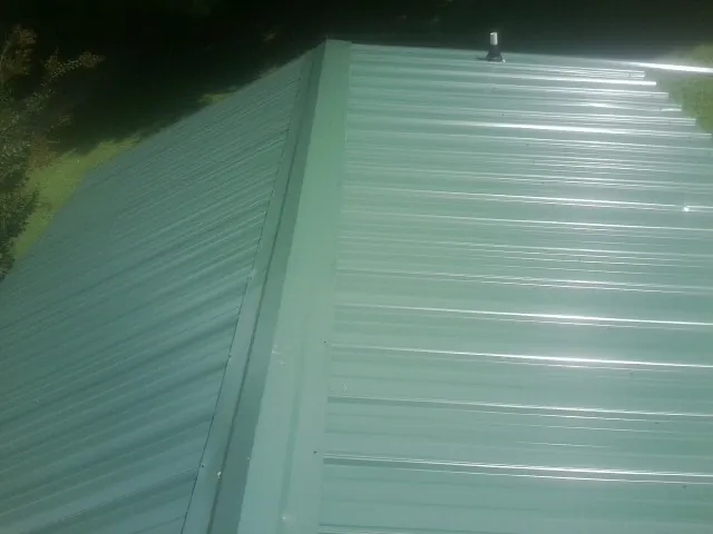 New green metal panels meeting at the ridge of a roof — Flat Roof Repair work by our crew in Lowman