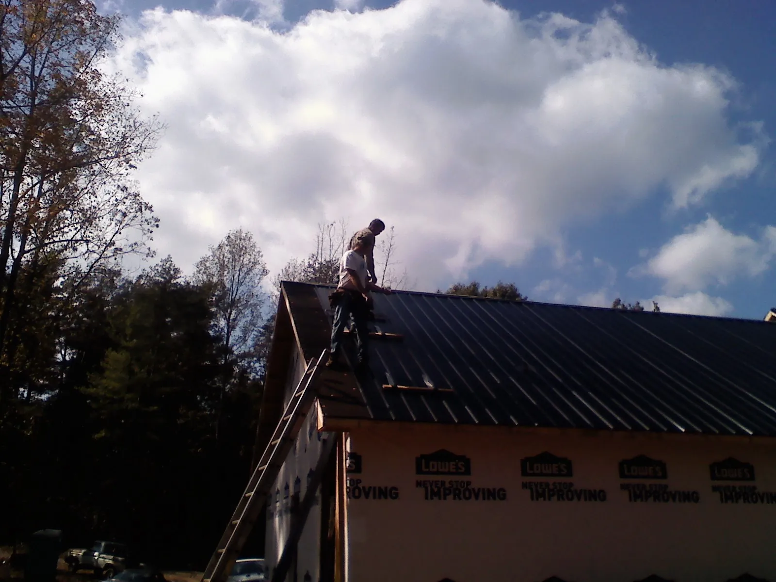 Roofer fastening dark metal panels high against a cloudy sky, from a Roof Inspection job in Lowman