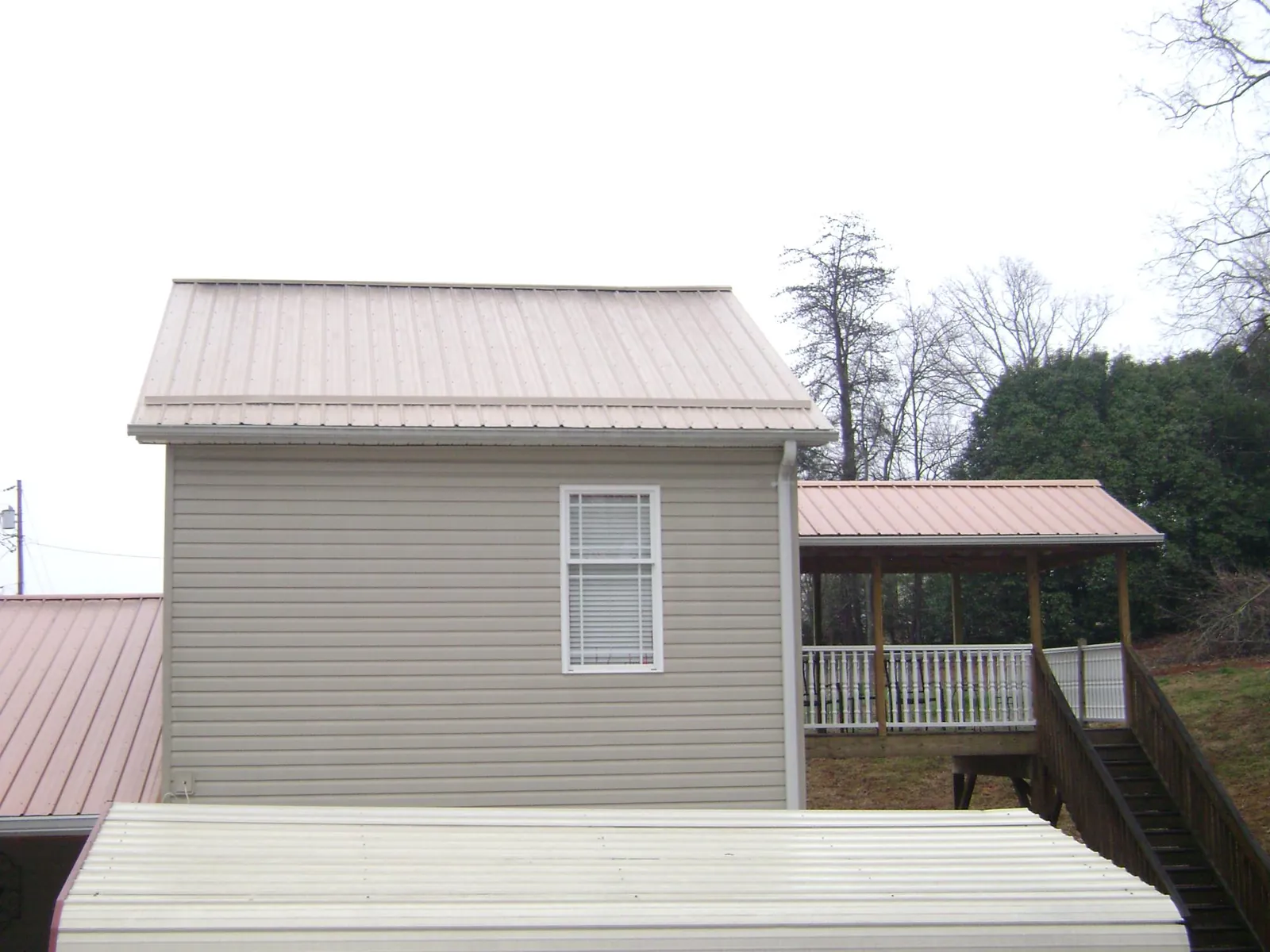 Tan metal roofs on a two story addition and attached porch, from a Roof Replacement job in Lowman